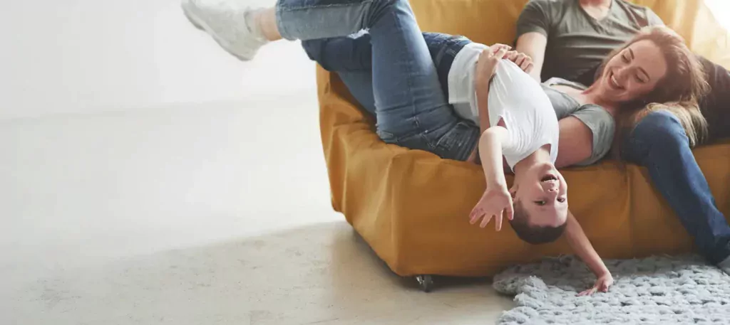 Famille qui rit dans un fauteuil, l’enfant la tête en bas